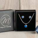 Birthstone gift set from Magnetic Mobility with blue Swarovski crystal necklace and matching stud earrings. Designed with magnetic backs for pain relief, elegantly displayed in a black box with Magnetic Mobility logo.