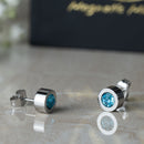 Magnetic Mobility Birthstone Stud Earrings featuring light blue Aquamarine Swarovski crystals. These earrings have a magnetic back and are designed for stylish pain relief, displayed on a reflective surface with Magnetic Mobility packaging.