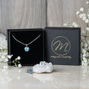 Magnetic Mobility March Birthstone gift set featuring a light blue aquamarine Swarovski crystal necklace and matching stud earrings. Each piece includes a magnetic back for stylish pain relief, beautifully presented with white flowers and a black branded box.