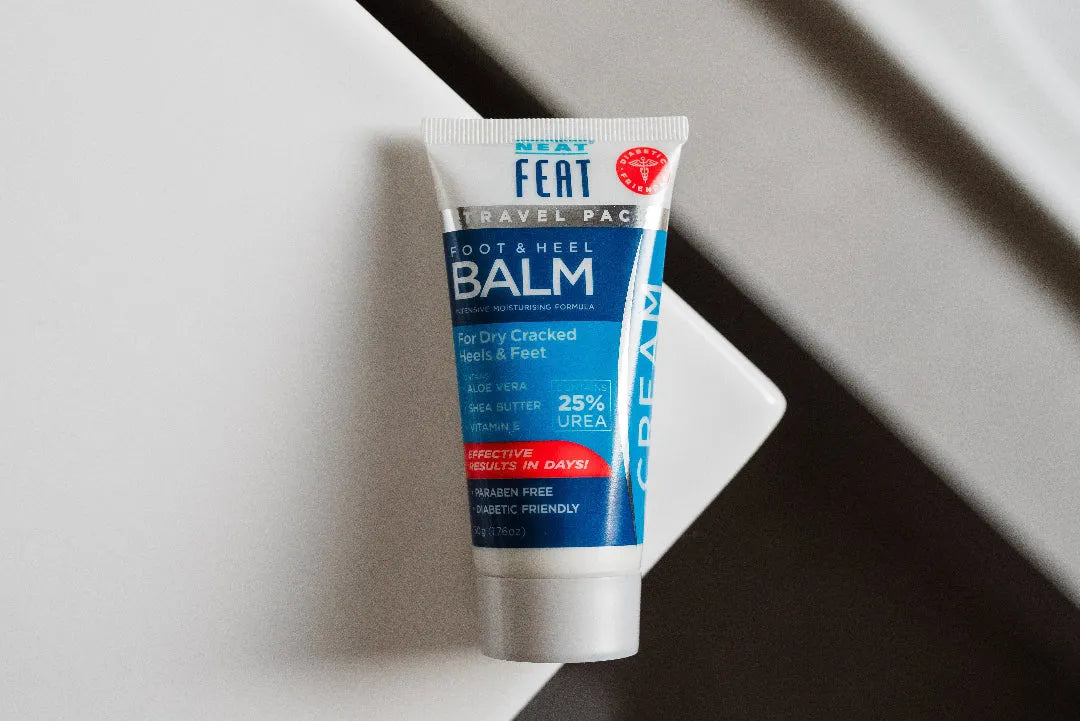 Bird's eye view of Neat Feat Foot & Heel Balm Travel Pack 50g tube, laying down on a white and black surface, featuring a grey cap and blue label.