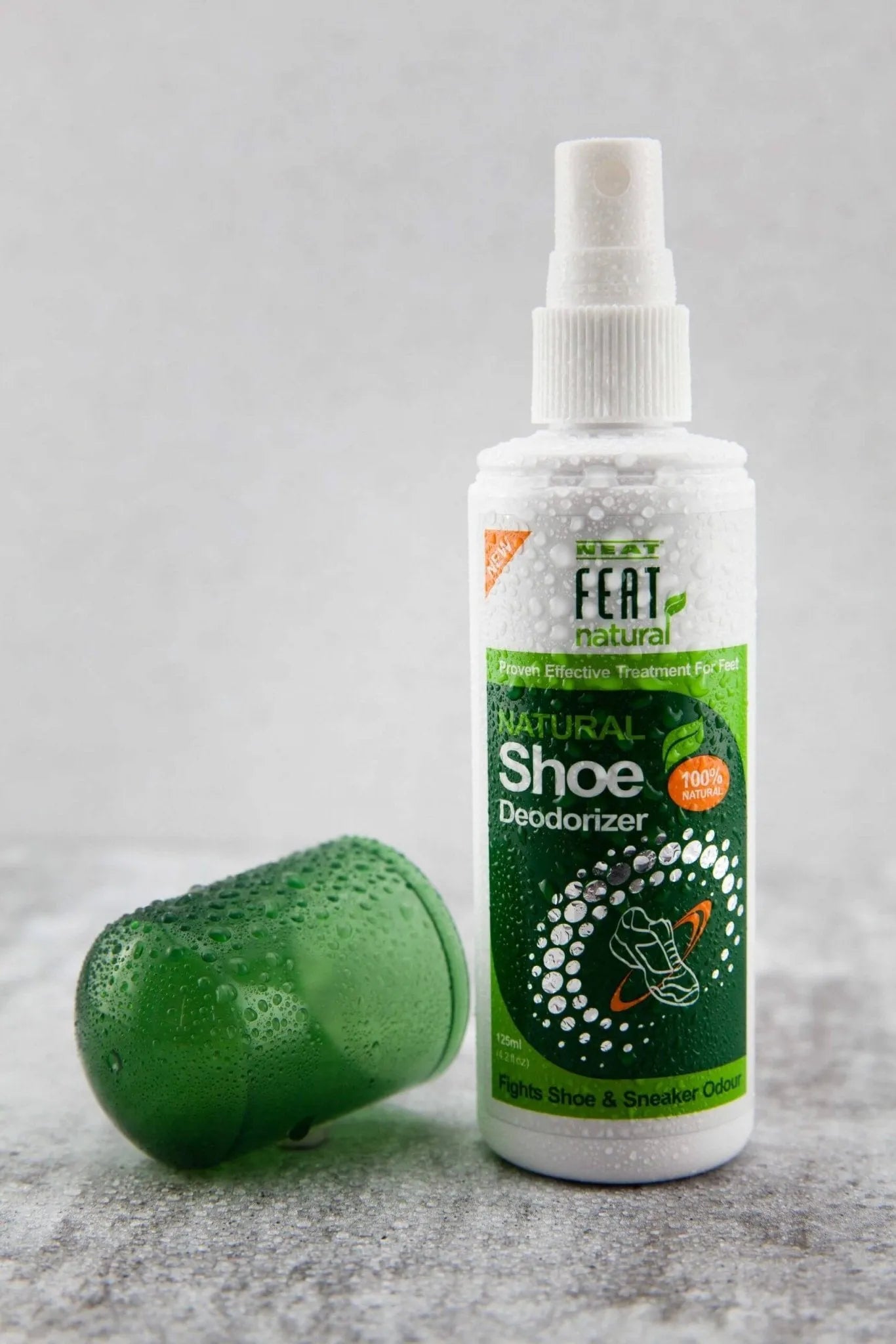 Front view of Neat Feat Natural Shoe Deodorizer with the cap removed, covered in water beads, creatively displayed on a sleek grey marble bench.